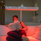 Person reading a book under a red light therapy lamp in a living room.
