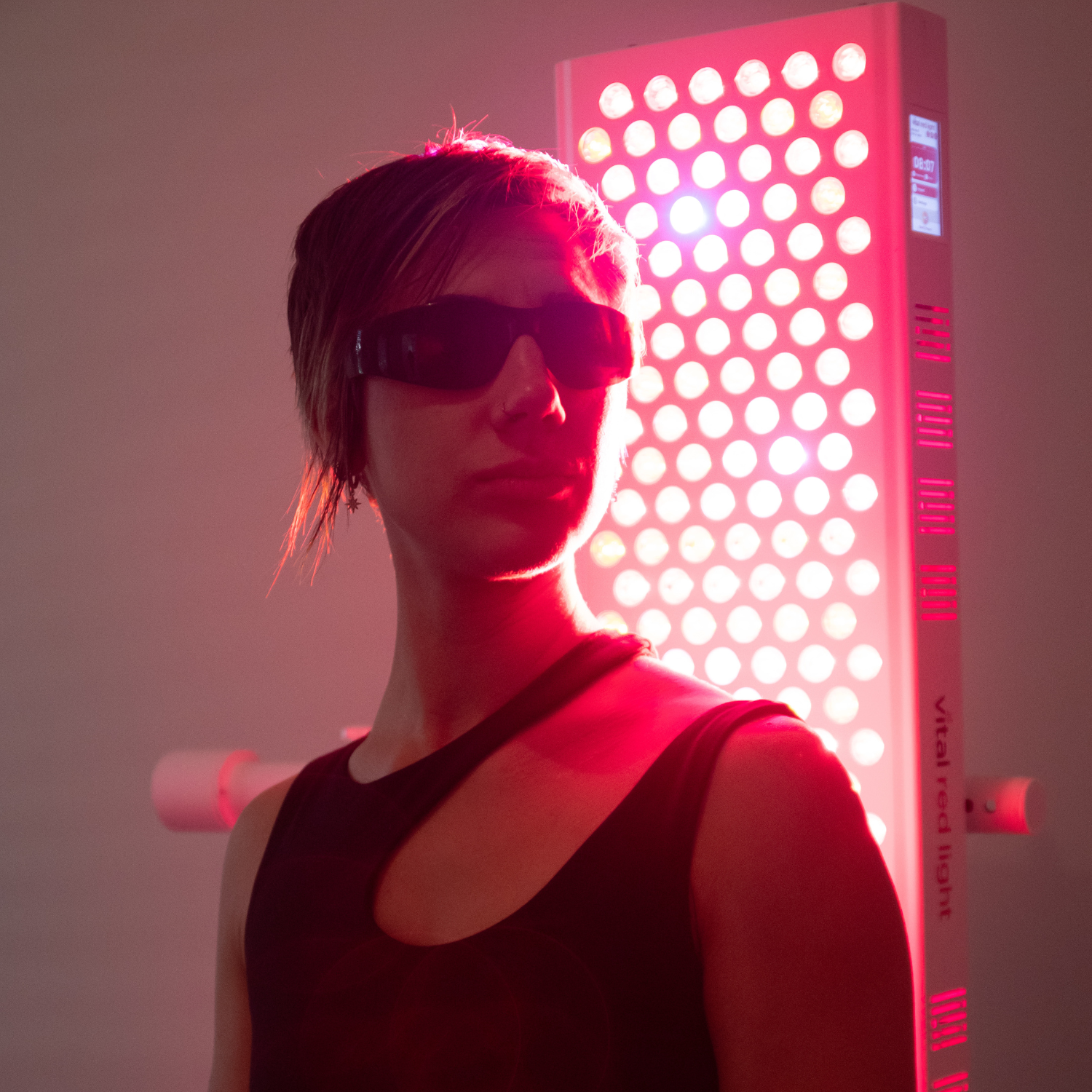 Person wearing sunglasses in front of a red light teraphy panel