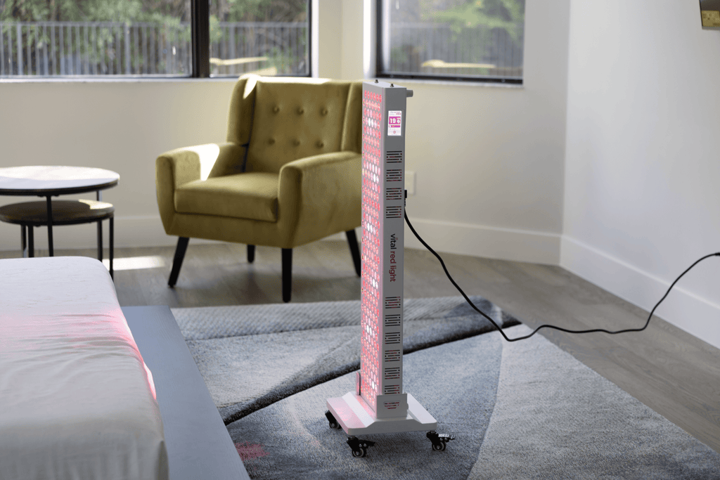 Tall rectangular red light teraphy device on a gray carpeted floor in a room with a yellow armchair and table.