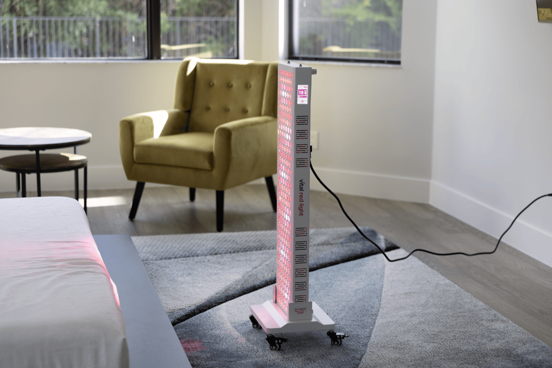 Tall rectangular red light teraphy device on a gray carpeted floor in a room with a yellow armchair and table.