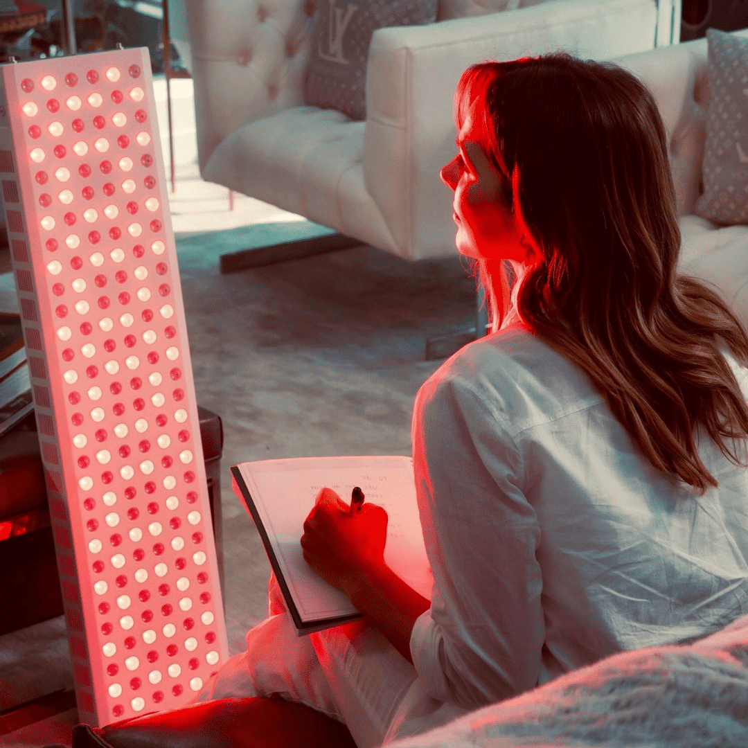 Person sitting on a couch with a red light therapy lamp next to them