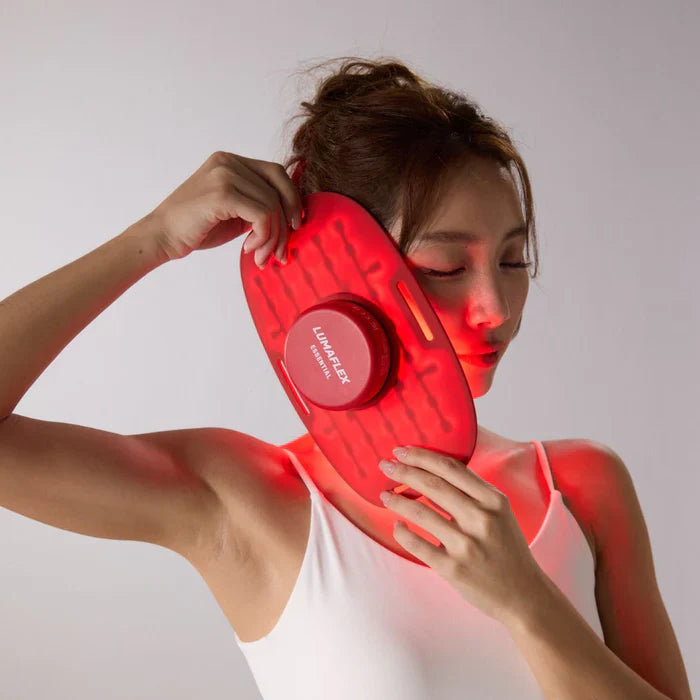 Woman using a red laser device on her shoulder against a gray background