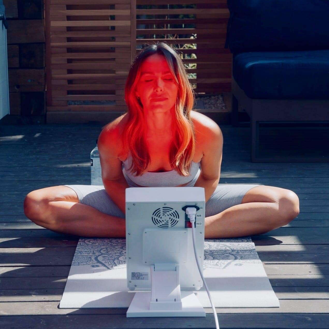 Person sitting on a mat with a device emitting red light for therapy or treatment.