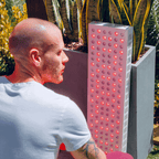 Man sitting next to a tall rectangular red light teraphy panel outdoors.