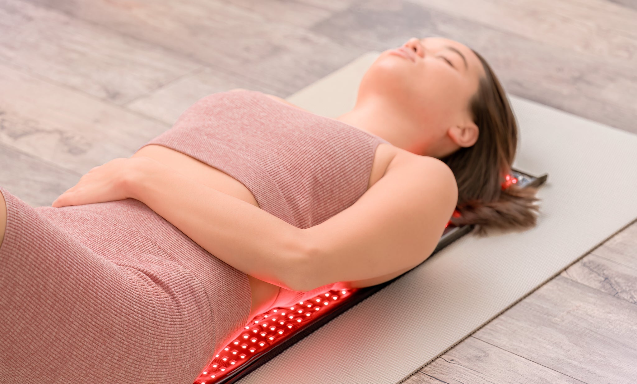 Woman lying on a red light teraphy mat on a wooden floor