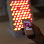Hand holding a controller with a digital clock app in front of a red light therapy device .