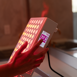 Hand holding a digital device with a red light panel and screen displaying numbers.