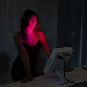 Person sitting in a dark room with red light teraphy device on a table.