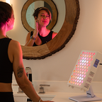 Woman using a LED light therapy device in front of a mirror